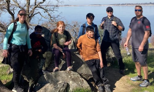Group of kids and adults sitting on rocks in front of folsom lake